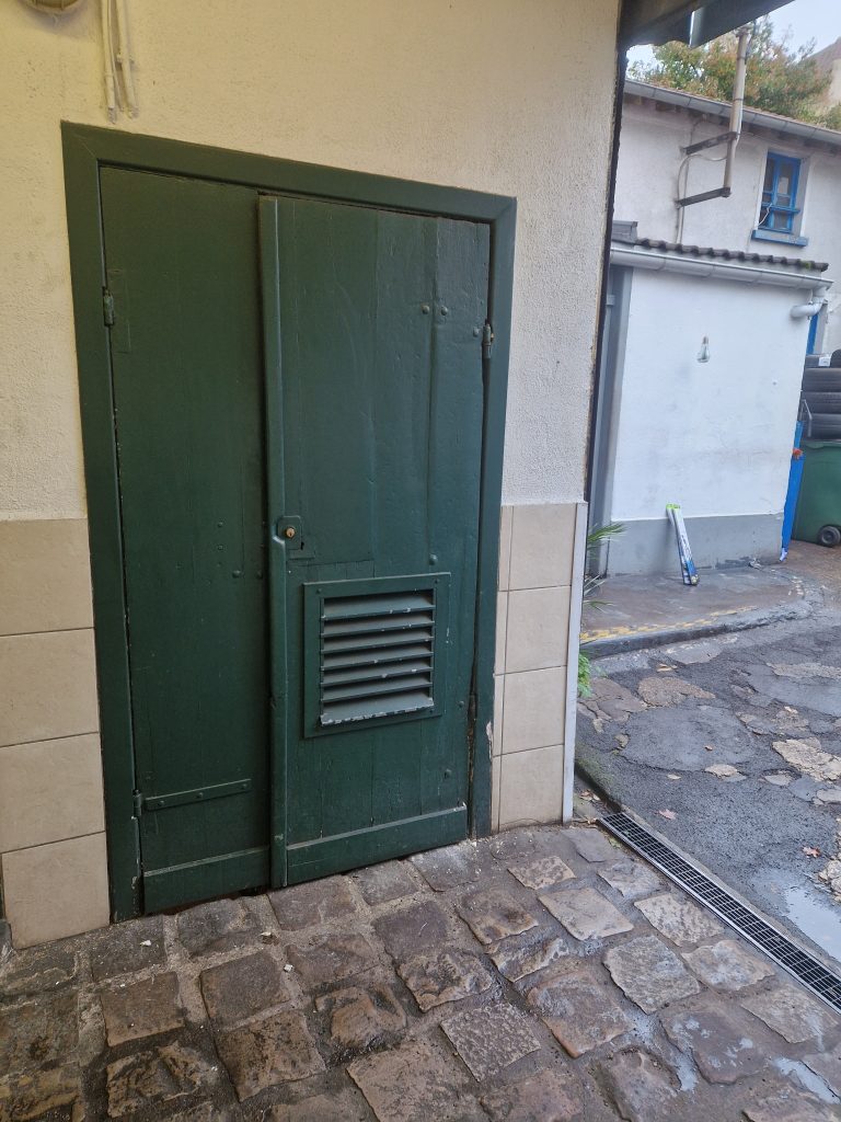 Ancienne porte bois local poubelles avant remplacement en copropriété.